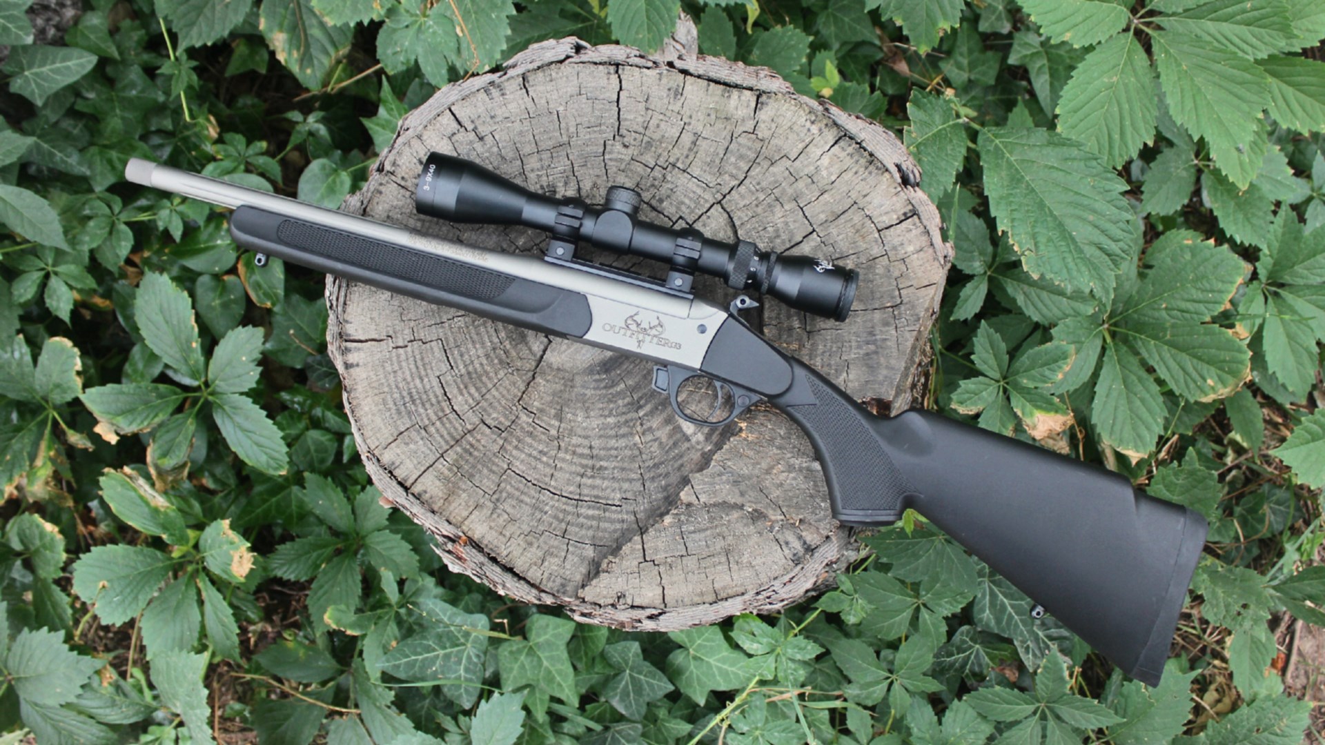 Traditions Outfitter G3 single-shot rifle left-side view shown on log with green leaves surrounding