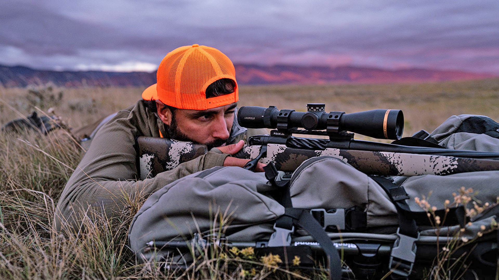 Man in an orange hat shooting the Weatherby Mark V High Country off a backpack.