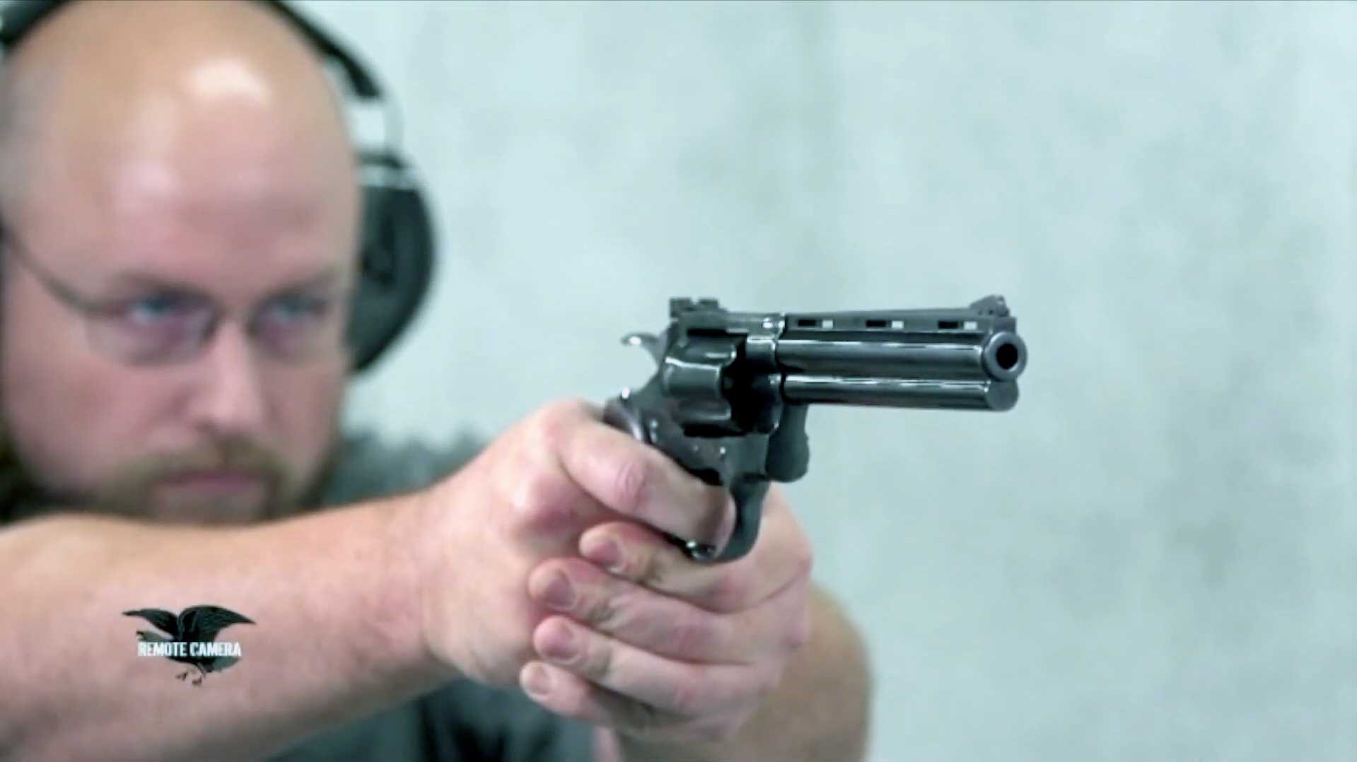 A man holding a blued Colt Python on a white indoor range, aiming it toward the target.