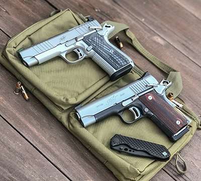 single-stack .45 ACP M1911 two guns left-side view stainless steel metal black knife shown on pistol bag on wood