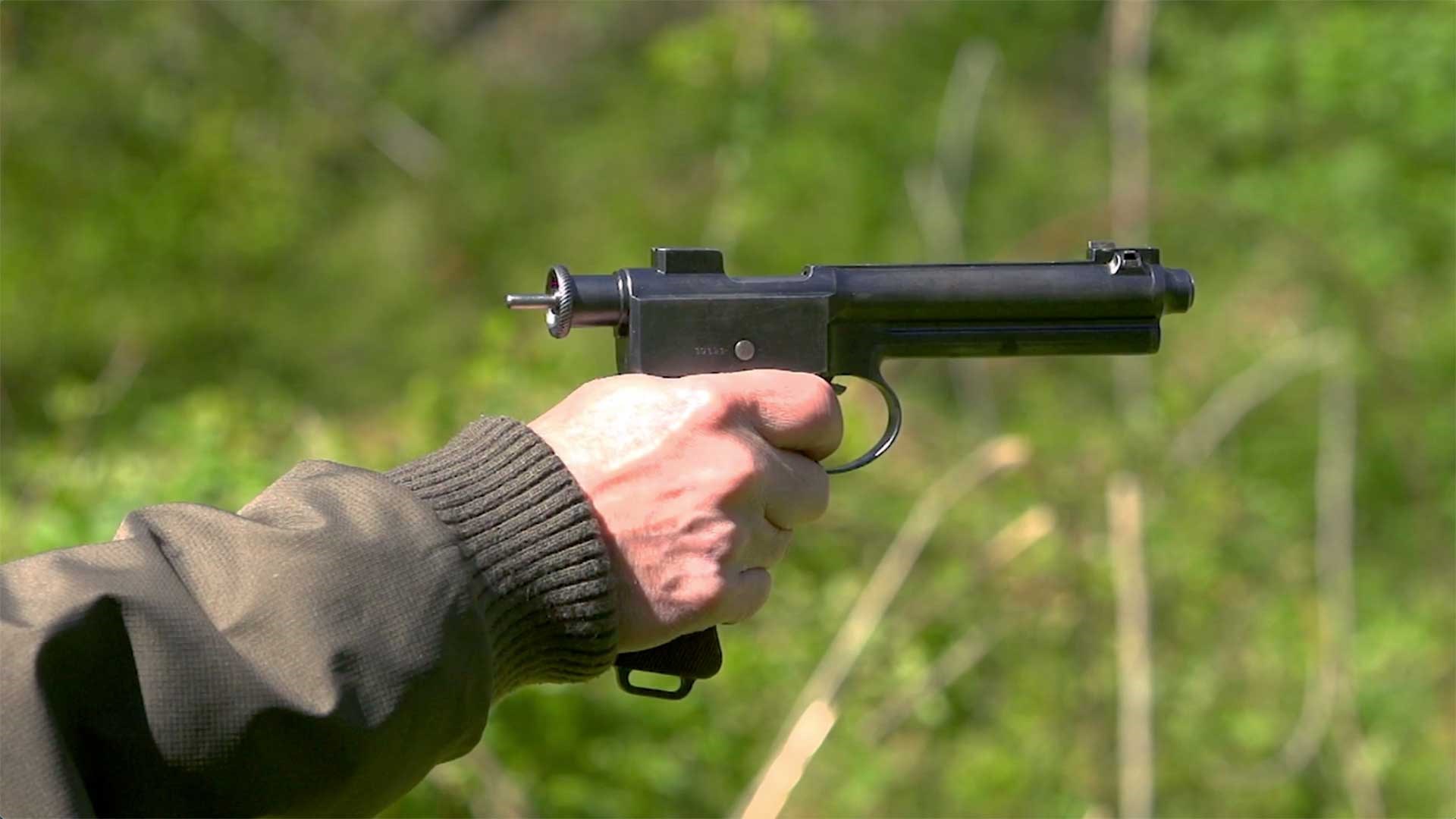 A man aims the M1907 Roth-Steyr pistol on a green outdoor range.