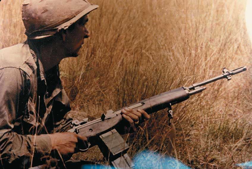 A U.S. infantryman walks through brush in Vietnam with his M14 rifle held in the low-ready position.