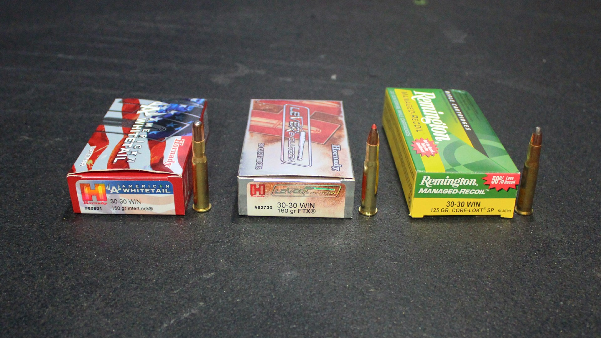 Hornady and Remington 30-30 Winchester ammunition boxes with cartridges standing to the right side of each of the three boxes