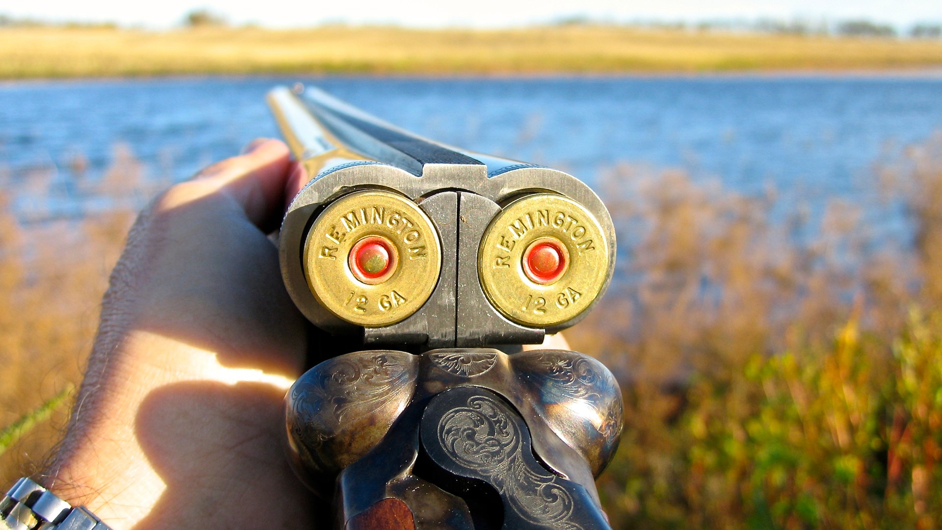 Side-by-side shotgun outdoors water background hunting hand engraving open action 12 gauge shotshells A side-by-side double provides the shooter with two instantaneous shots that can be quickly reloaded.