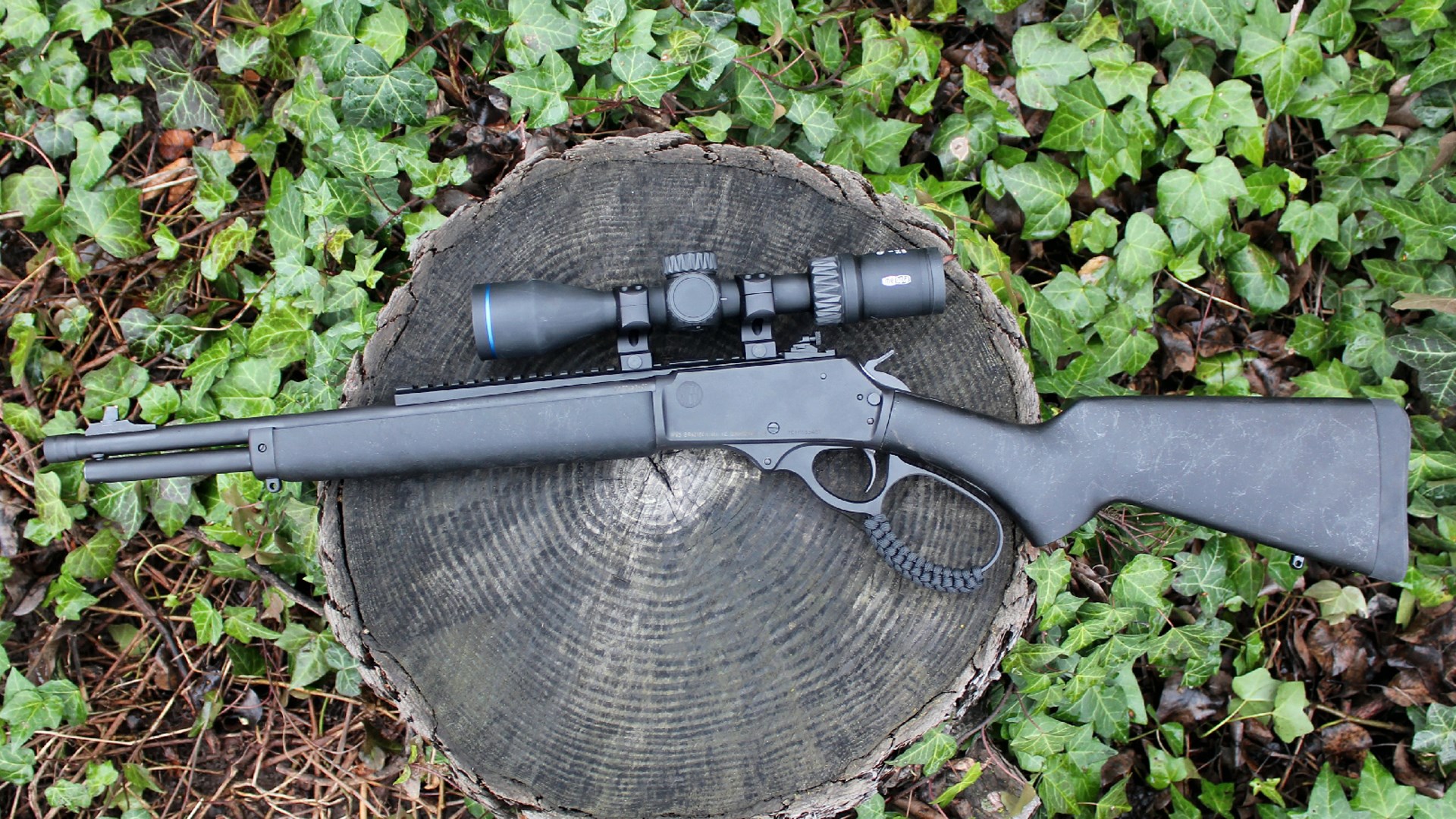 Rossi R95 Triple Black left-side view lever-action rifle shown with riflescope on stump outdoors green ivy background
