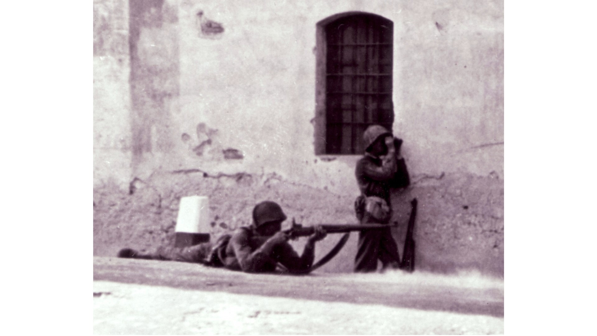 A rare appearance of the .30 caliber M1917 “Enfield” rifle in combat during WWII. This US artilleryman takes aim on the streets of a Sicilian town. NARA