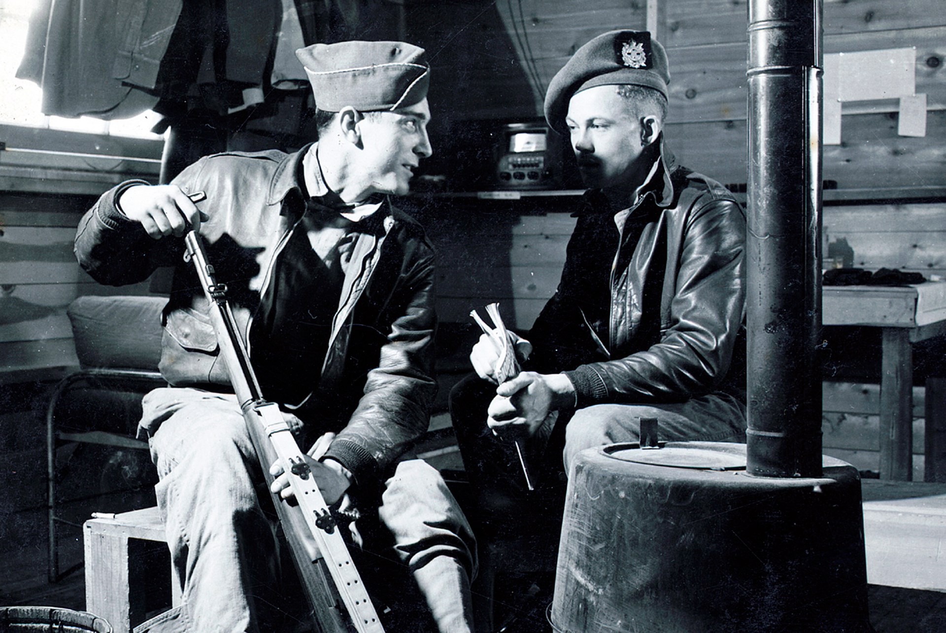 men in barracks cleaning rifle next to multi-fuel stove cabin soldiers training