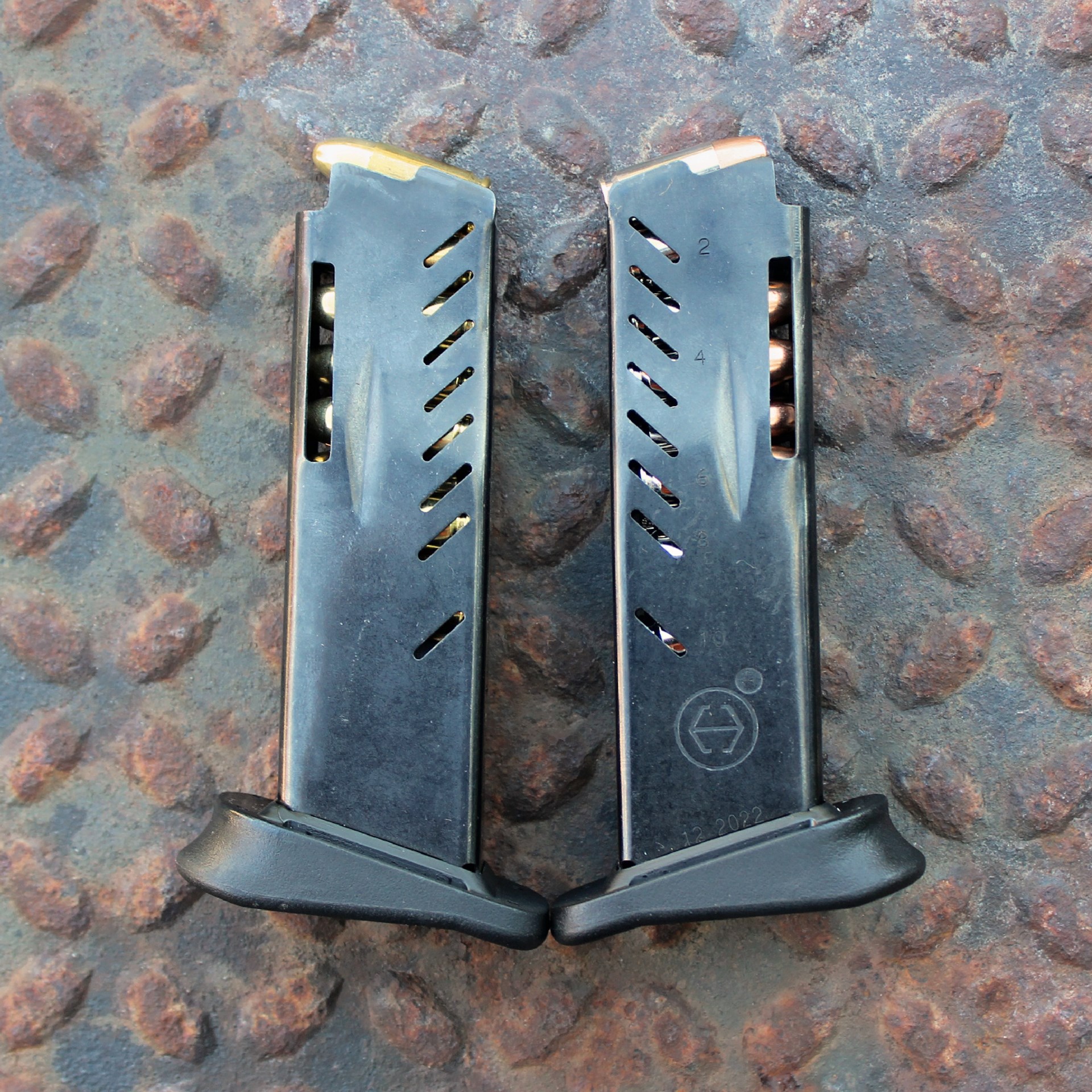 Hi-Point Firearms YC9RD handgun magazines two mags opposing each other with ammunition black steel lightening cuts shown on rusty metal treadplate background
