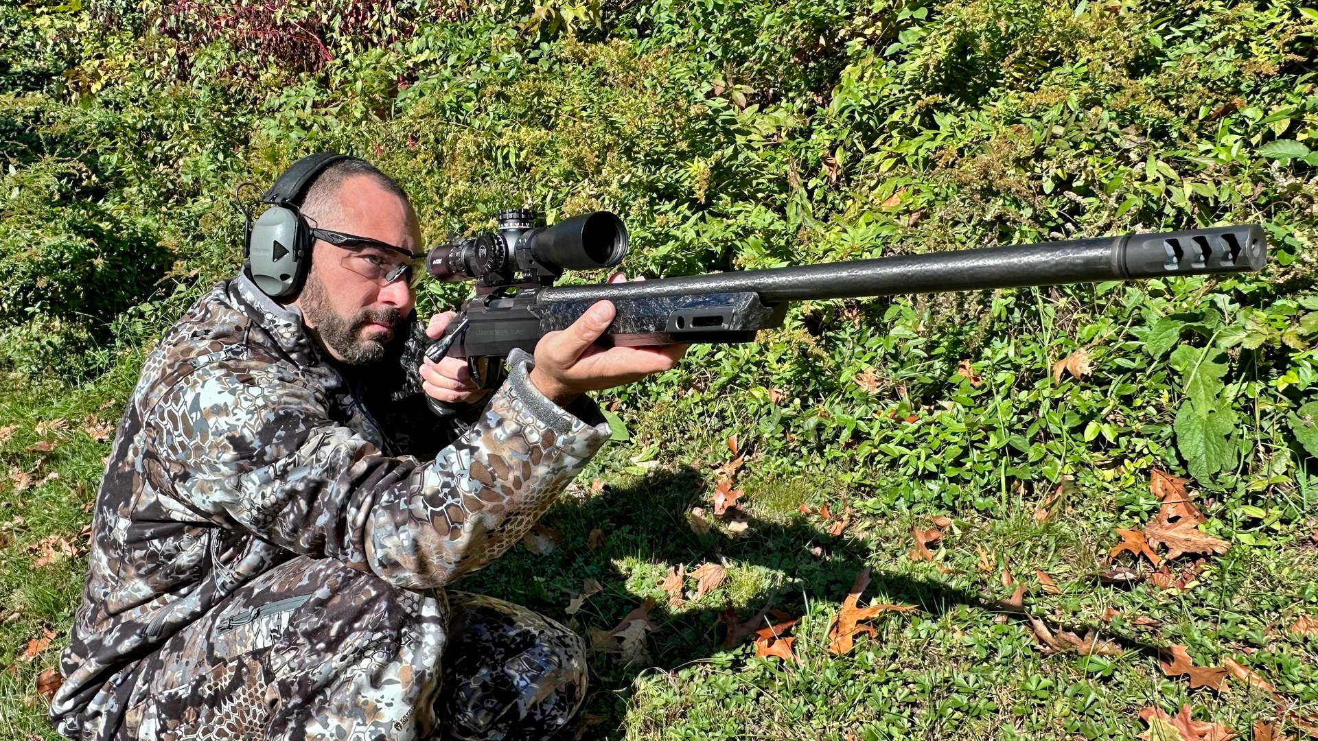 Man kneeling wearing camouflage outdoors bushes background bolt-action christensen arms modern hunting rifle carbon fiber