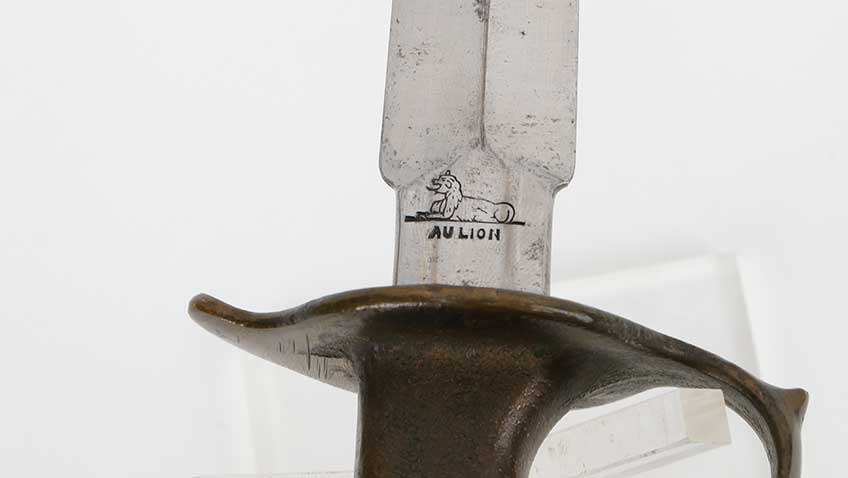 Close-up view of pommel with lion stamping shown on white background.