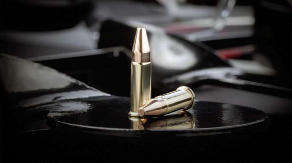 Two Winchester .21 Sharp cartridges resting on a black steel plate.