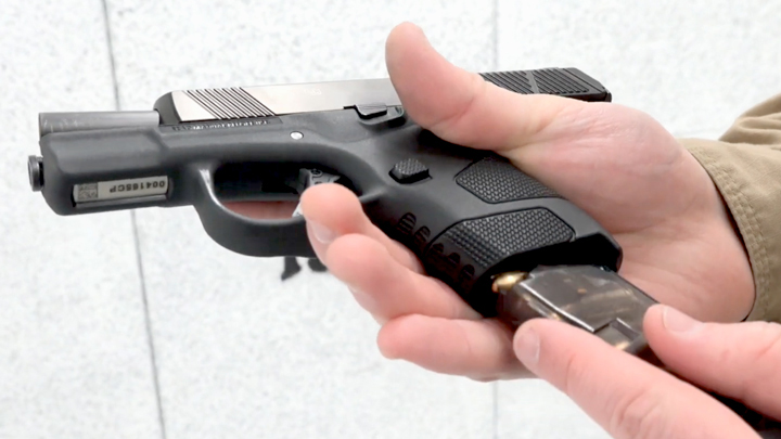 Mossberg pistol in hand being loaded on shooting range.
