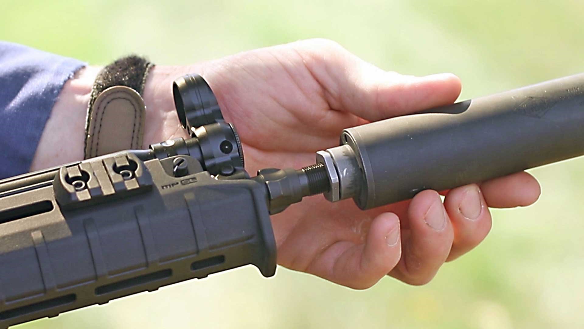 A user's hand mounting a suppressor onto an MP5.