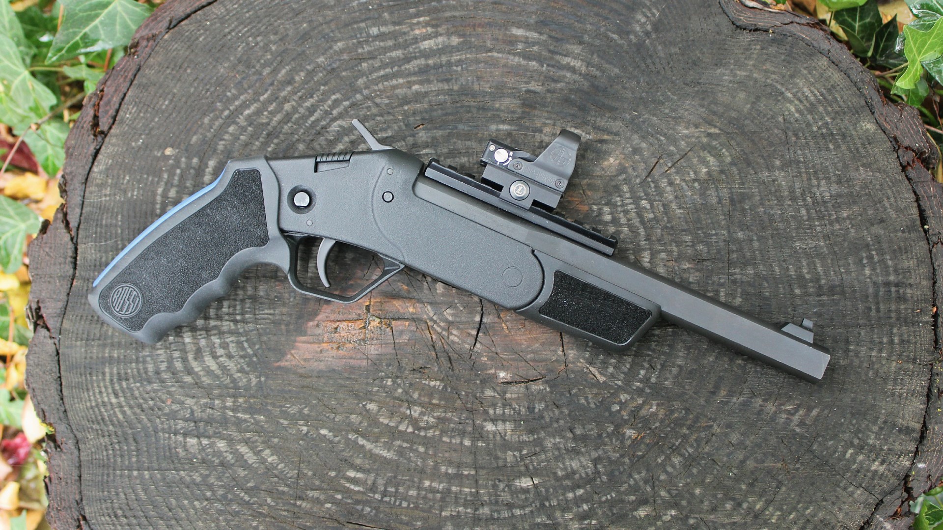 right-side view of black rossi brawler handgun single-shot multi-use handgun shown outdoors with red-dot optic on round log with leaves