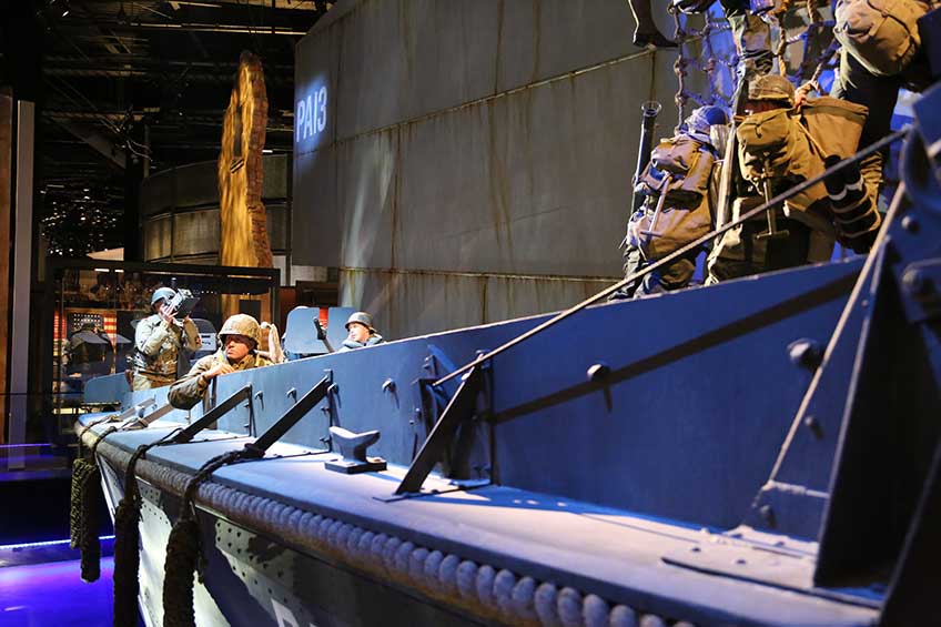 The blue-painted Higgins Boat in the National Museum of the U.S. Army, shown with U.S. soldiers climbing down rope netting into the landing craft.