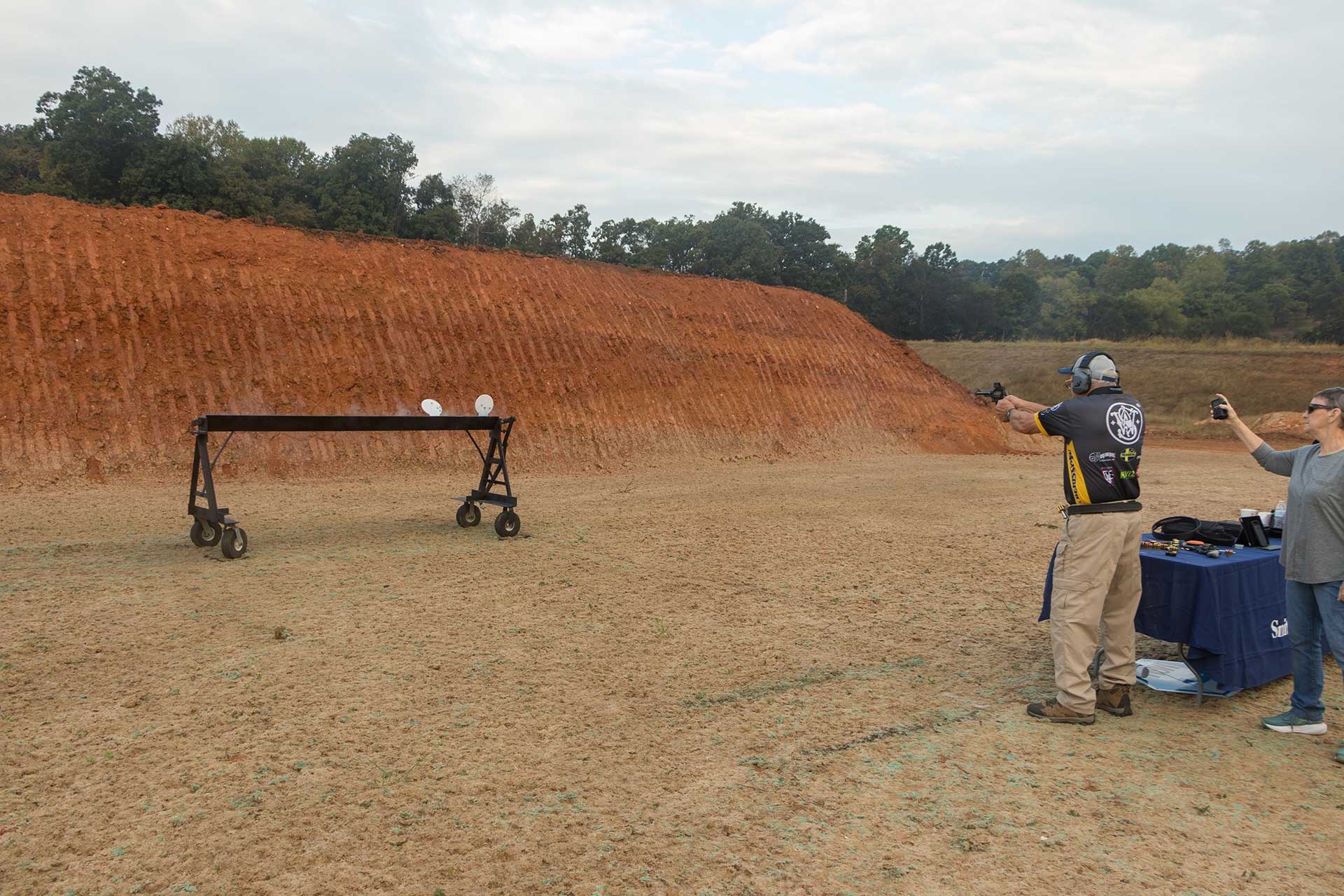 Jerry Miculek aims at white steel plates with a Smith & Wesson revolver on a dirt range.