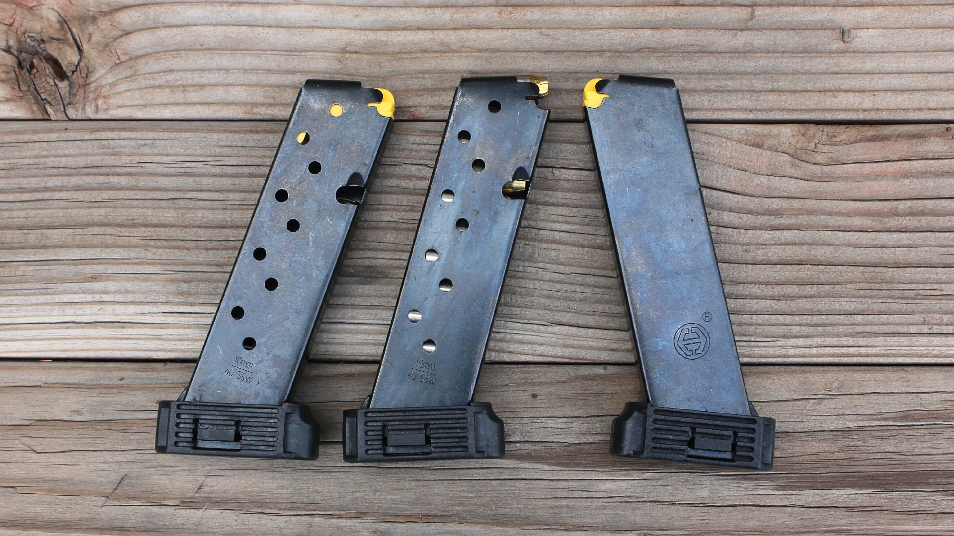 three detachable box magazines with yellow followers inserted and extended plastic baseplates shown on wood boards