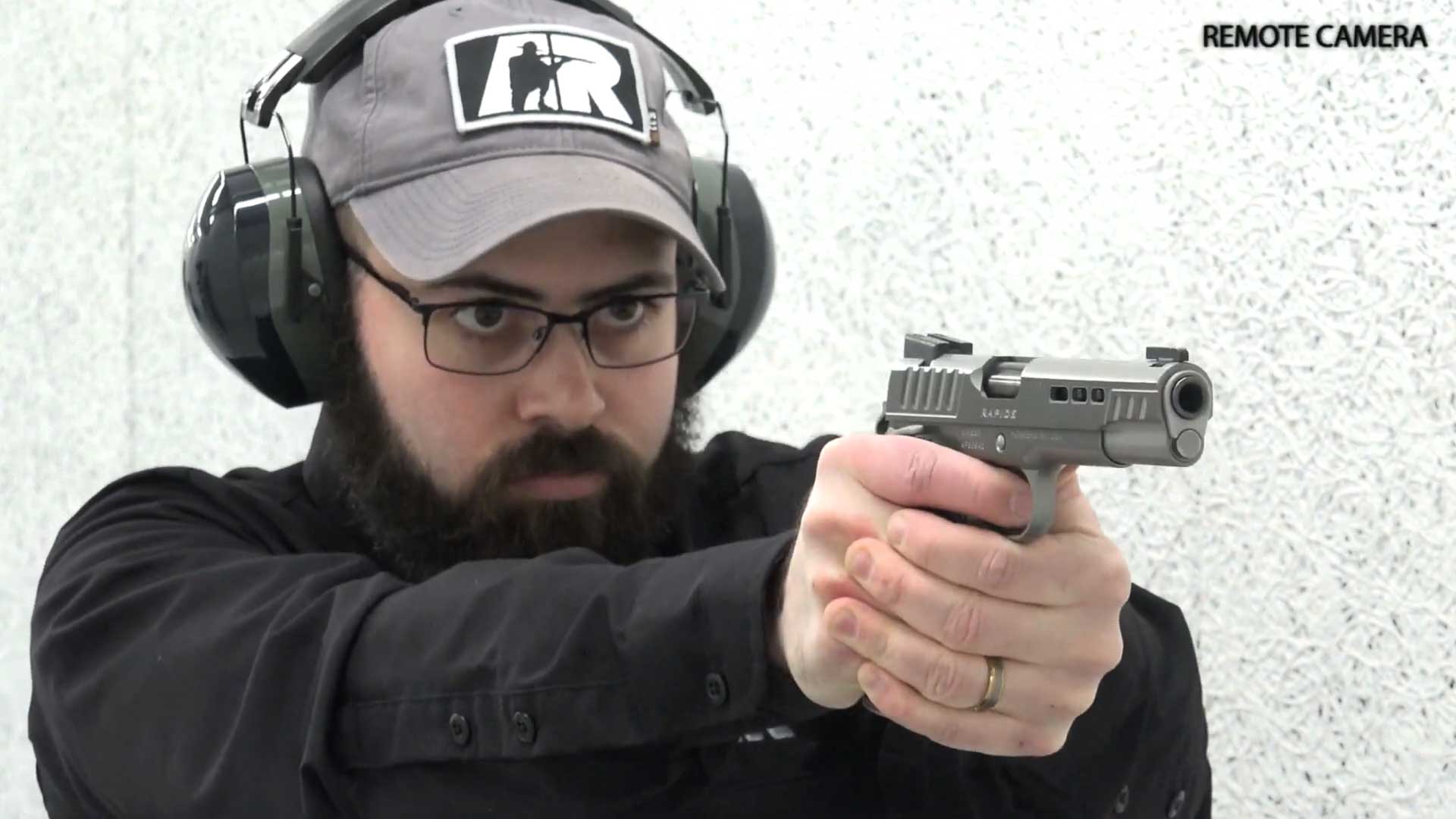 man wearing black shirt ballcap earmuffs on shooting range with handgun kimber america rapide black ice 10 mm video remote camera