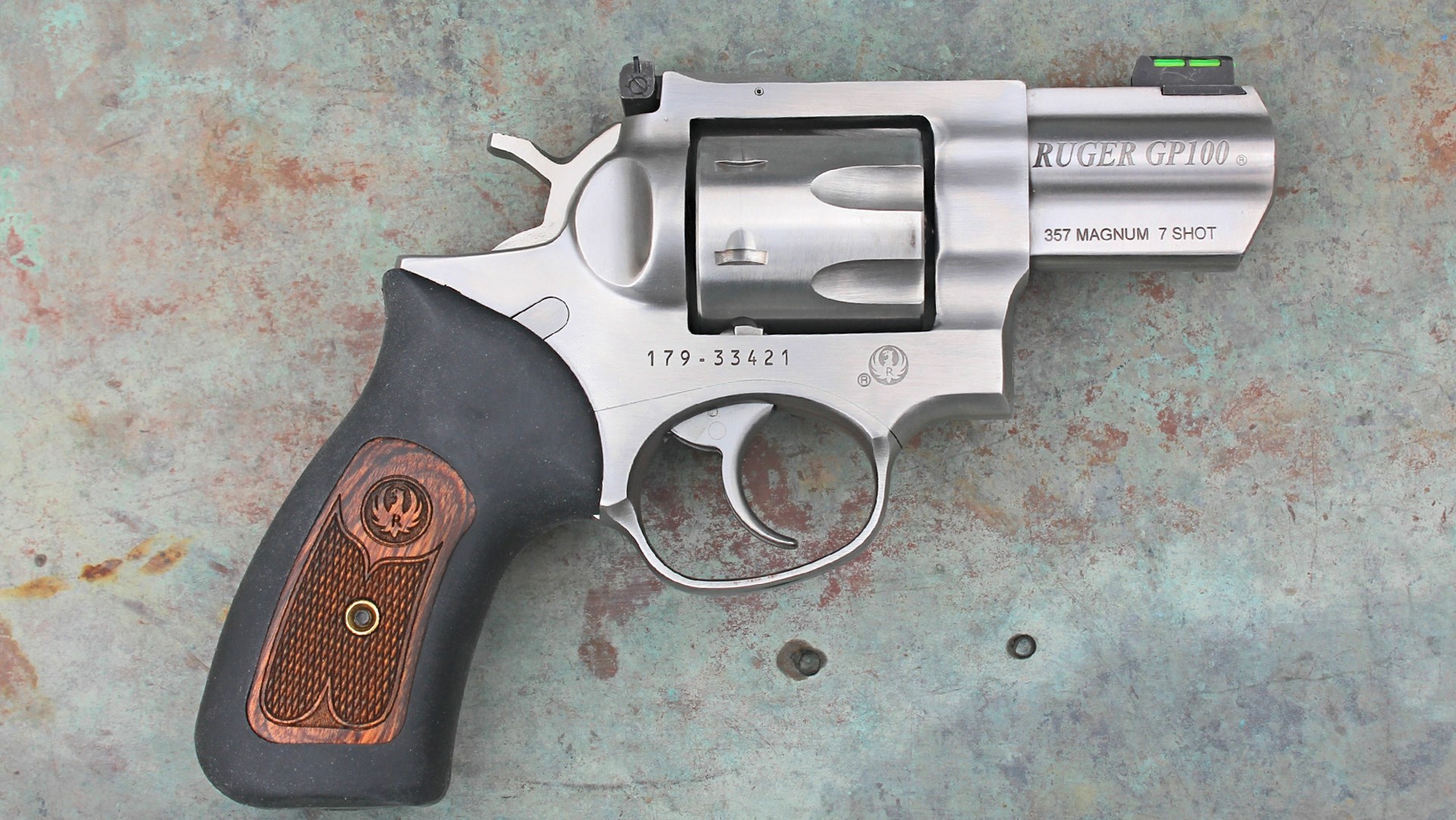 Ruger GP-100 seven-shot revolver right-side view stainless steel gun rubber grips wood concrete background