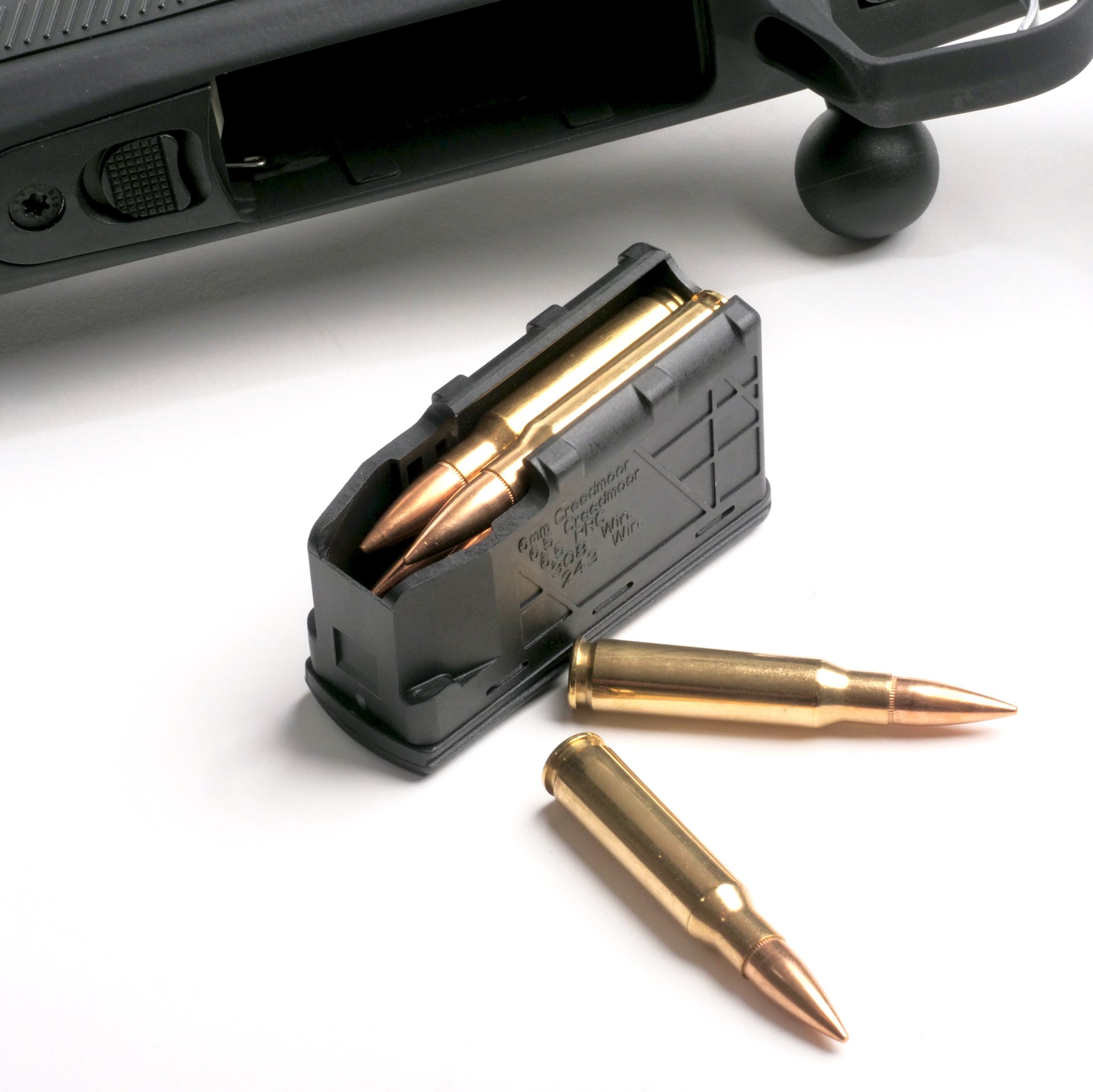 CZ 600 bolt-action rifle in background with black polymer magazine loaded with .308 Win. cartridges and two on white table