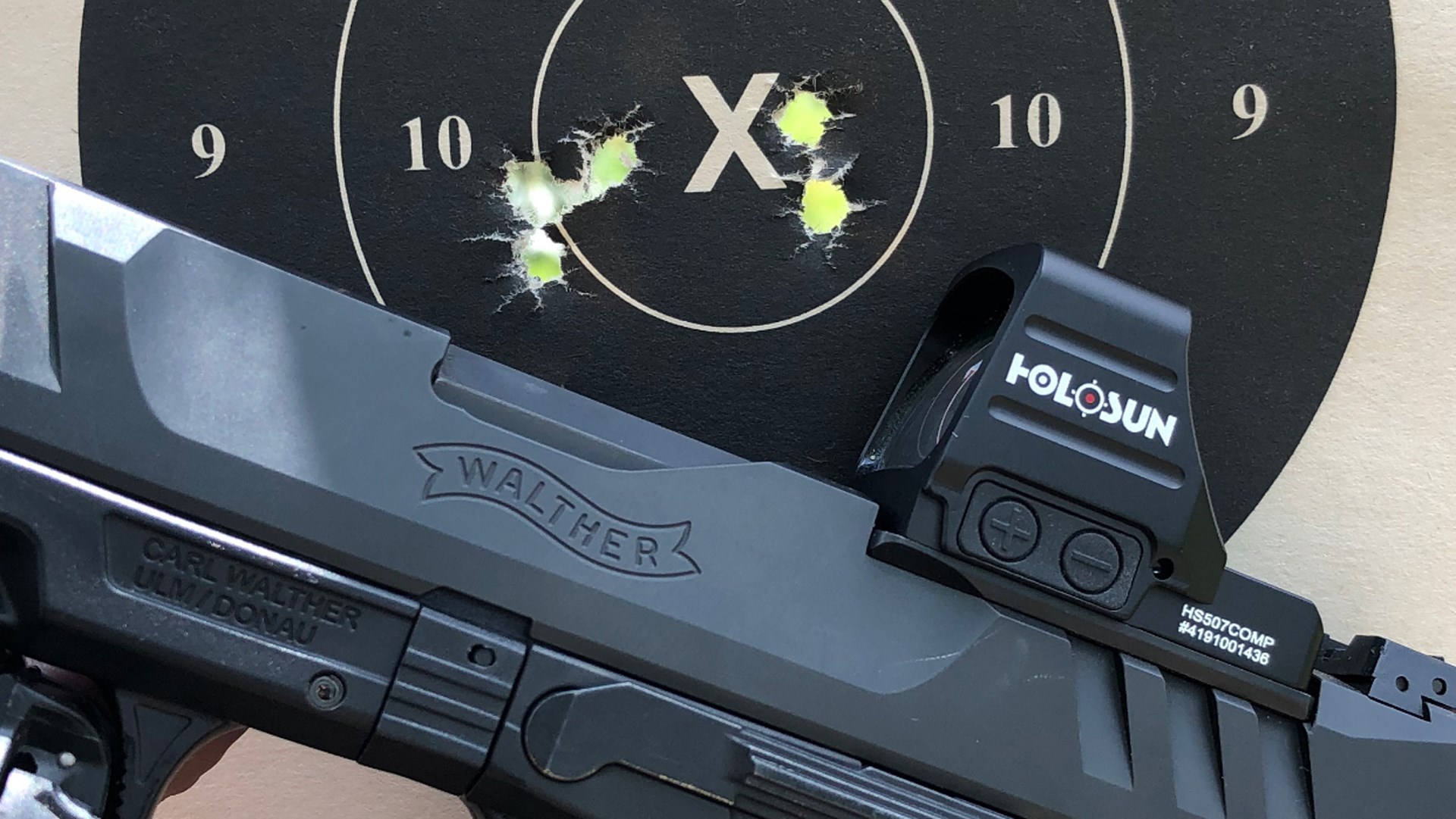 Walther pistol with Holosun 507 Comp red-dot optic attached in front of bullseye target holes X numbers rings