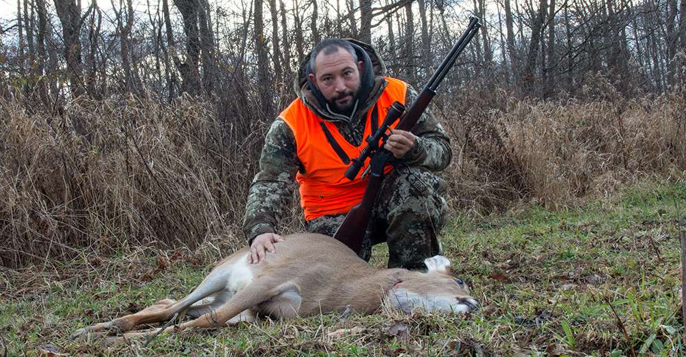 author on whitetail hunt holding rifle outdoors lever-action orange vest trees field woods whitetail deer