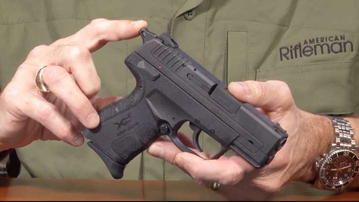 Right-side view of Springfield XDe pistol in hands with man&#x27;s finger pointing to the gun&#x27;s hammer.