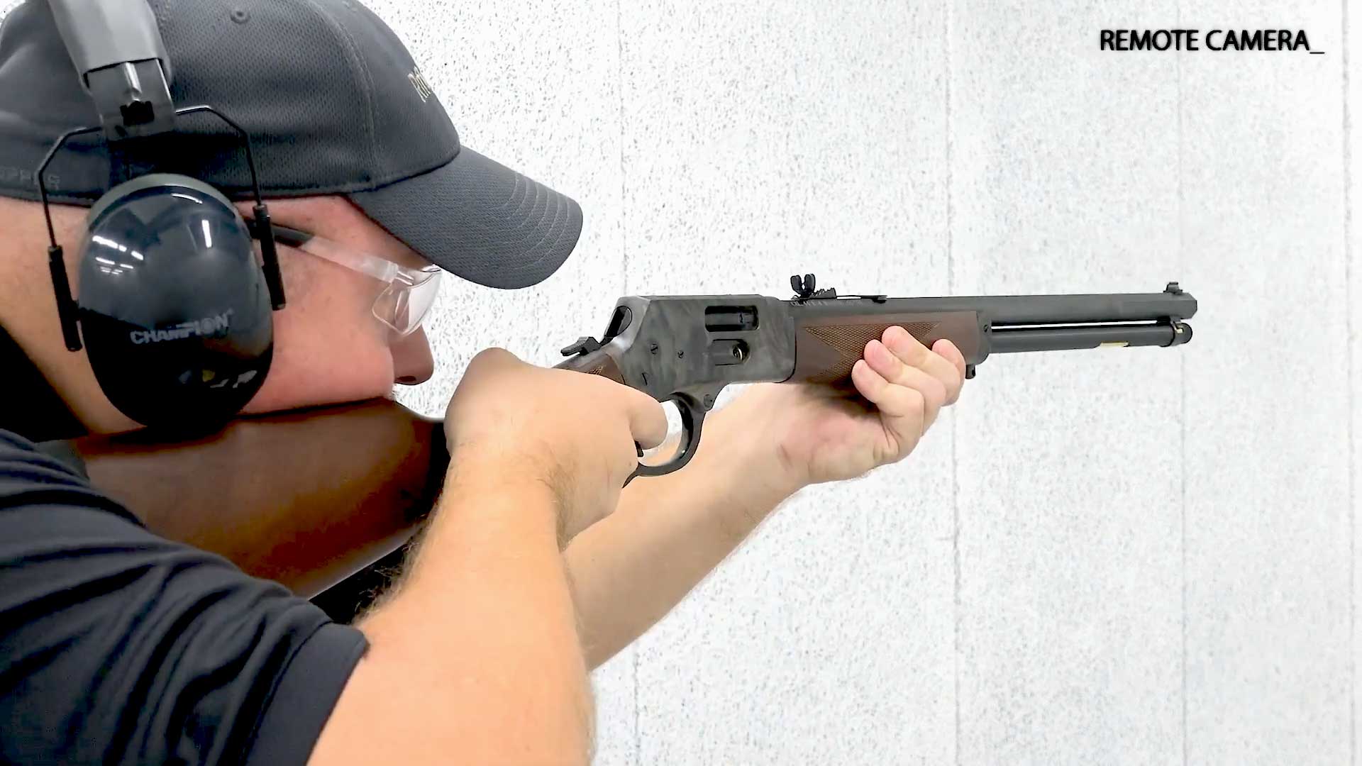 man wearing black shirt ballcap and earmuffs shooting lever-action rifle wood metal steel