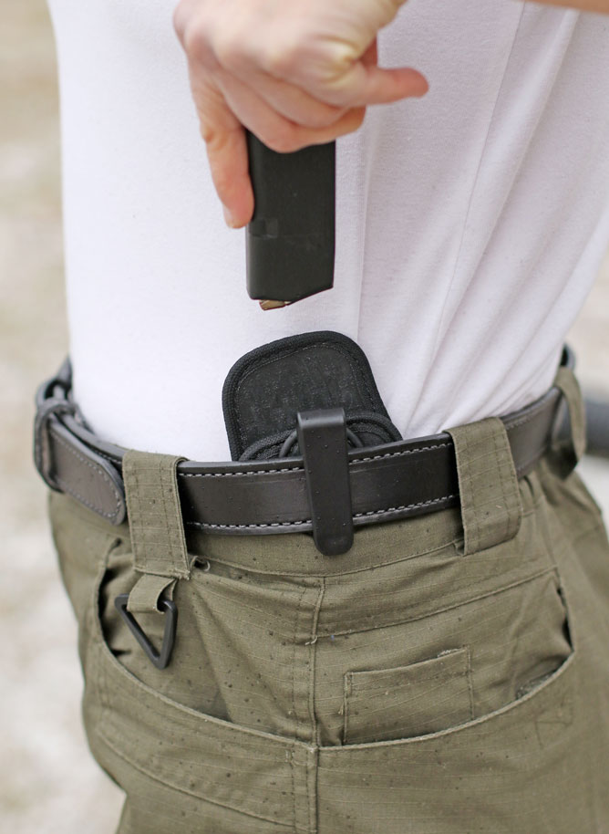 Woman in white shirt drawing a pistol magazine from a Tactica Grip Mag Carrier held inside the waistband of pants.