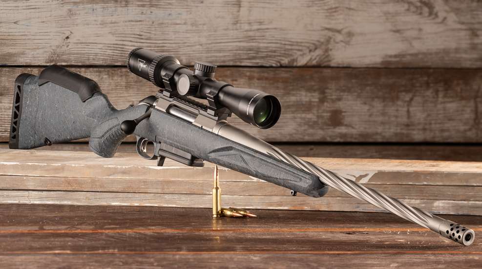 Ruger’s Generation II American Rifle shown with riflescope on wood with ammunition dynamic quartering angle spiral barrel gray stock