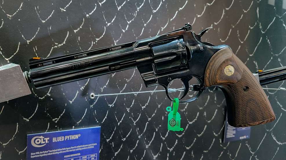 Left-side view Colt Python blued-steel revolver wood stocks grips walnut gloss finish gun on wall peg blue sign with blurred text