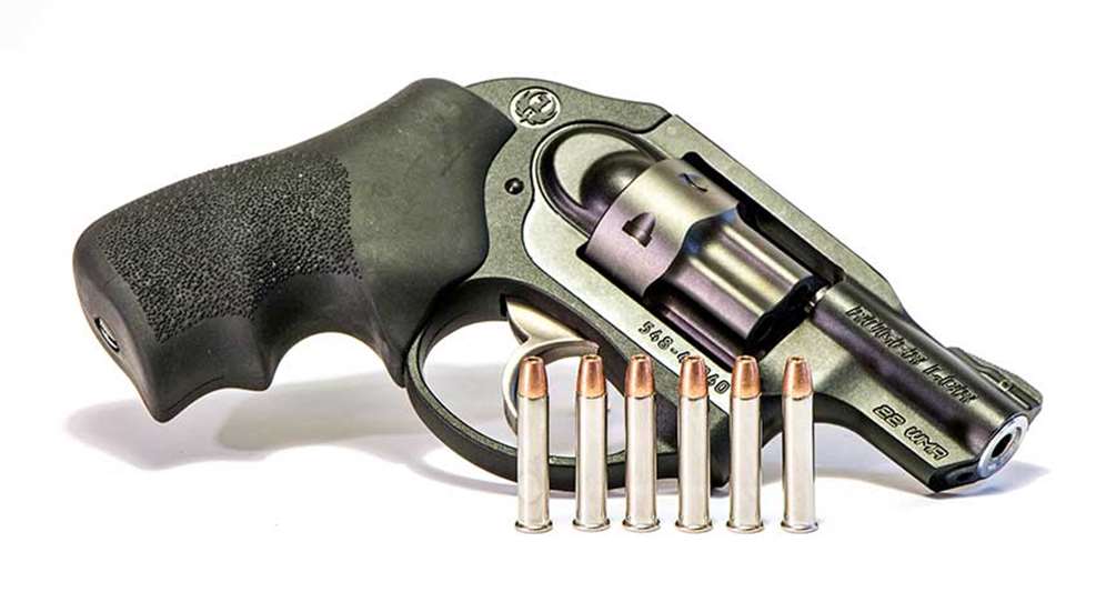 A Ruger LCR revolver laying on a white table with six .22 Magnum rounds standing up in the foreground.