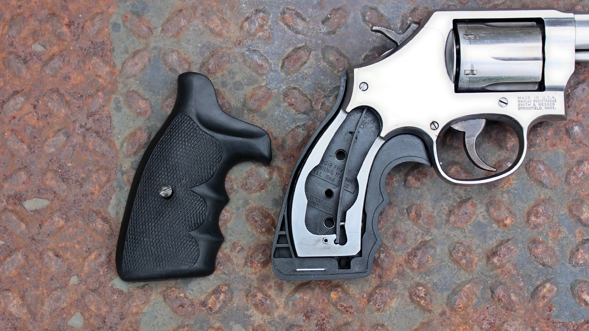 Smith & Wesson stainless steel revovler right-side view shown with stock panel removed and square-butt frame exposed shown on rusted treadplate background
