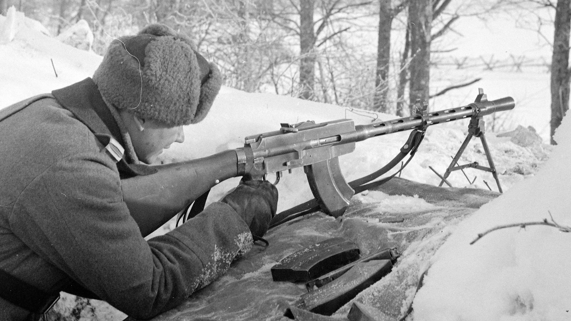Finnish soldier firing M/26 light machine gun in snow woods with bipod and spare magazines