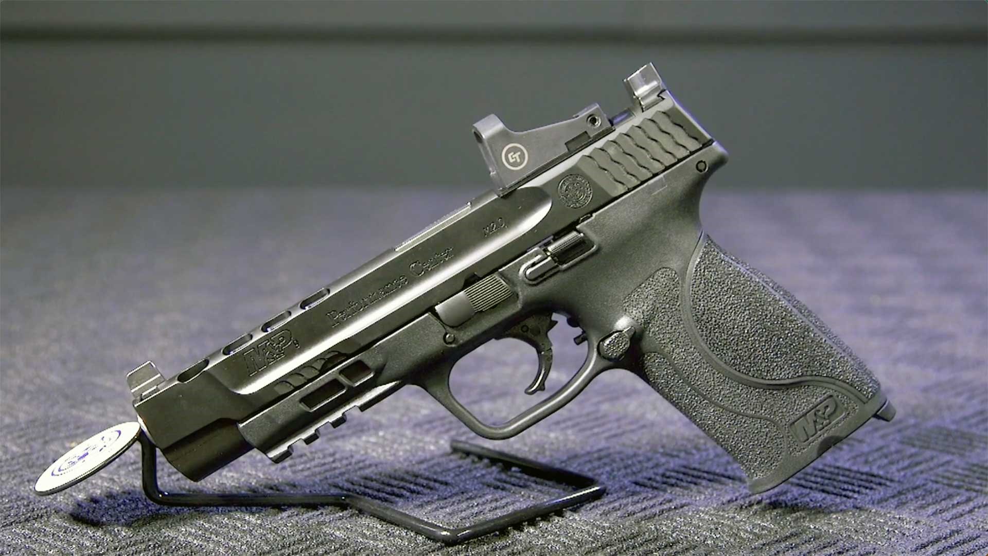 A Smith & Wesson Performance Center M&P pistol with a red-dot optic shown on a textured black surface.