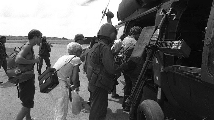 Evacuees board a UH-60 Black Hawk helicopter mounting a stripped-down M60D machine gun, featuring spade grips and a canvas bag to catch ejected spent casings.