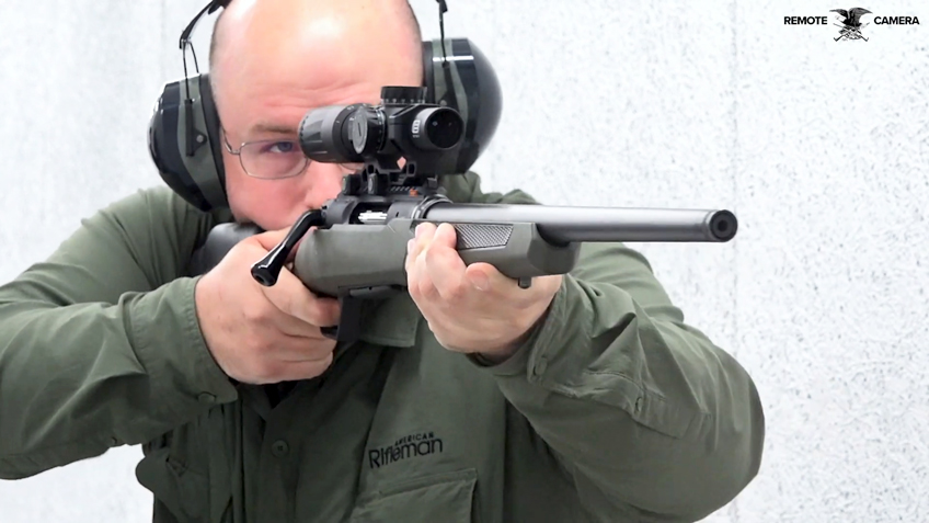 Man wearing ear muffs glasses green shirt shooting a green rifle on white target range