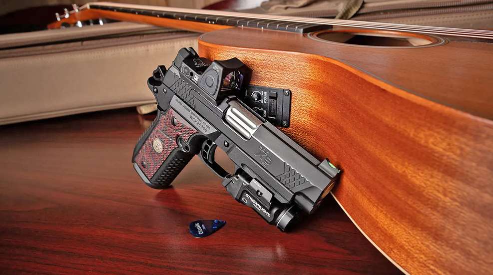 A Wilson Combat EDC X9 2.0 leans up against a guitar laying on a wooden tabletop.