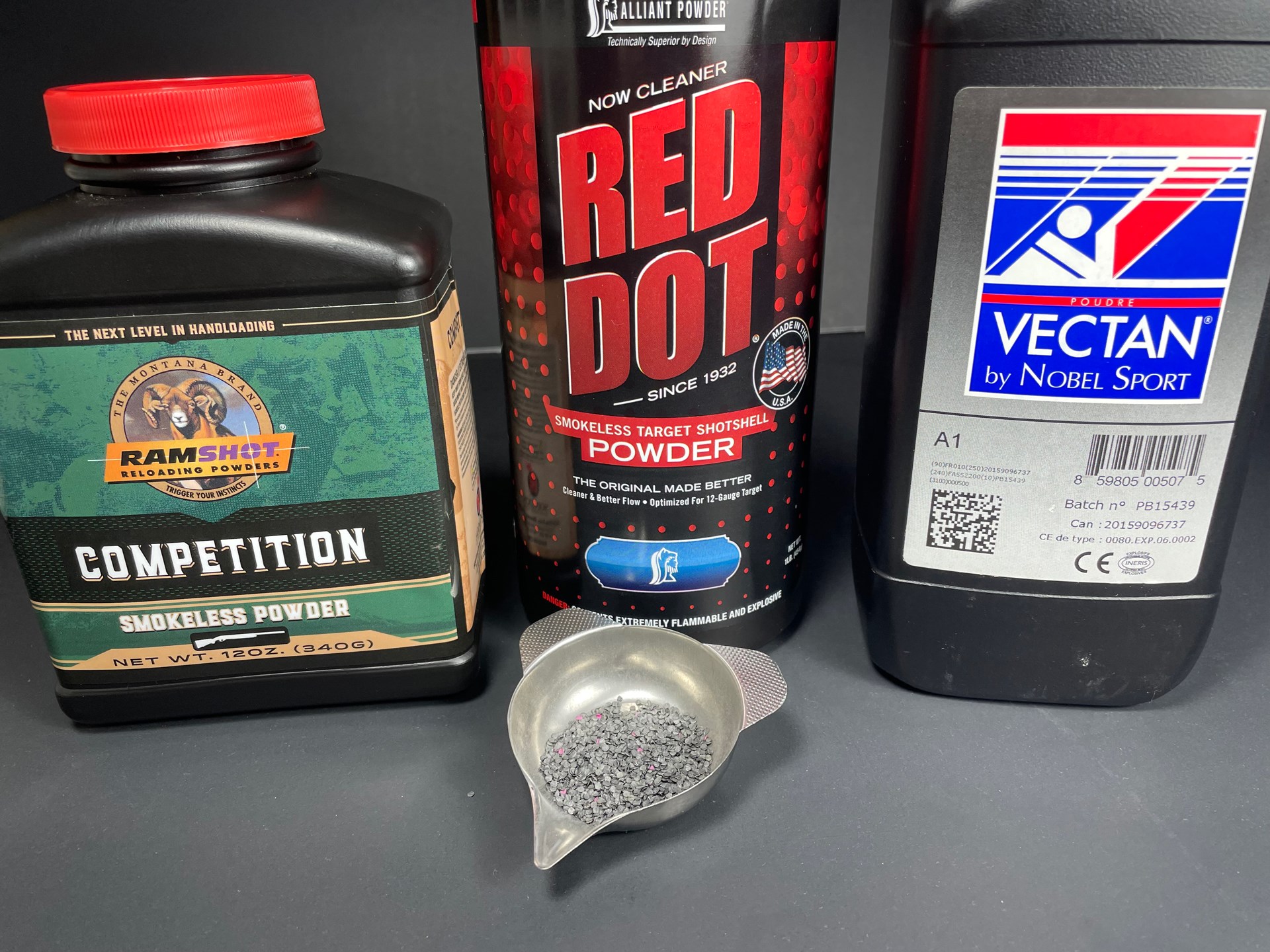 Flake-shaped propellants, such as Alliant Red Dot (c.) shown here, are typical of what’s used in shotshells. These sometimes pull double-duty for handgun ammunition.