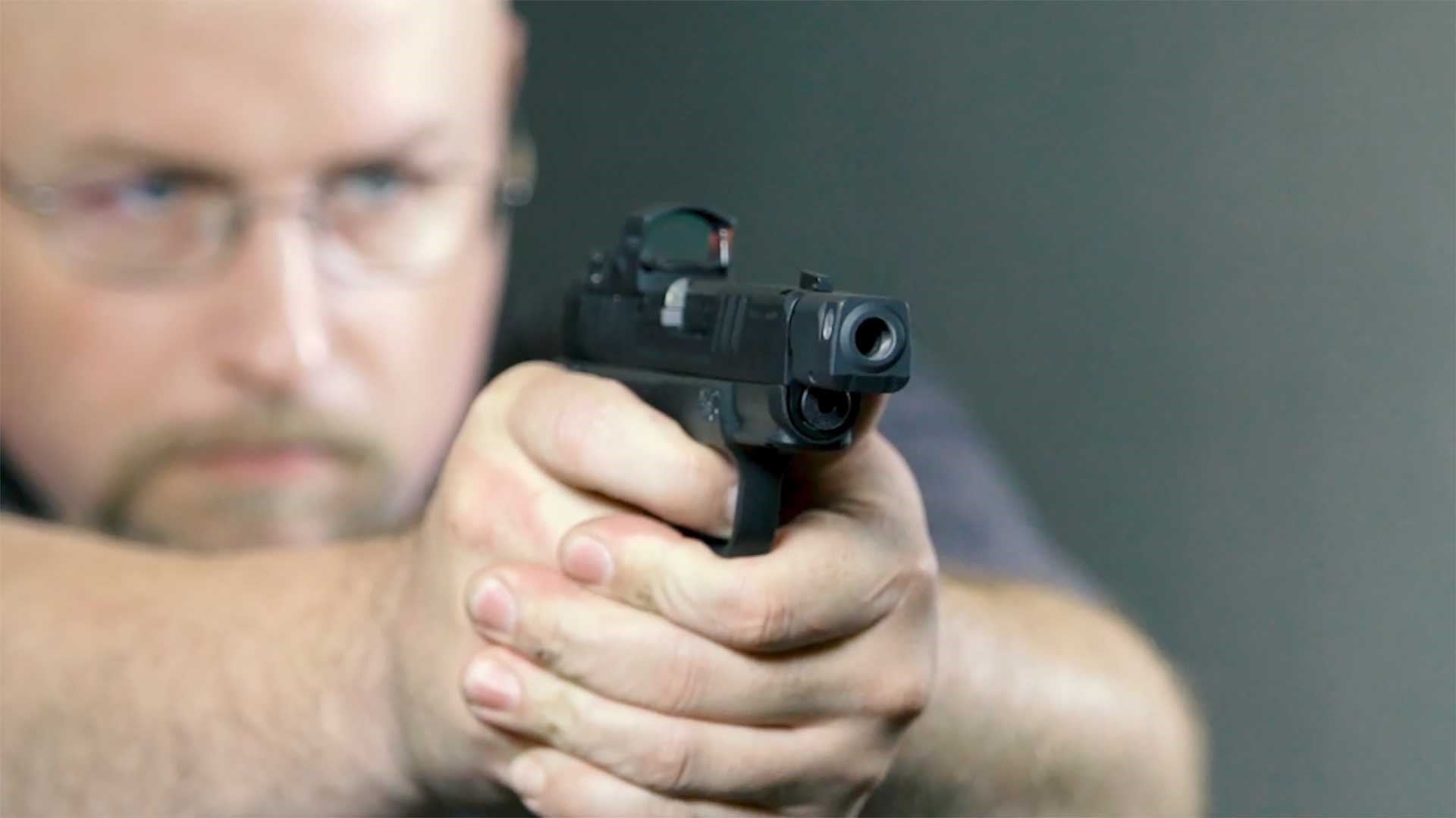 man on shooting range with Springfield Armory Hellcat RDP pistol black gun with red-dot optic indoors