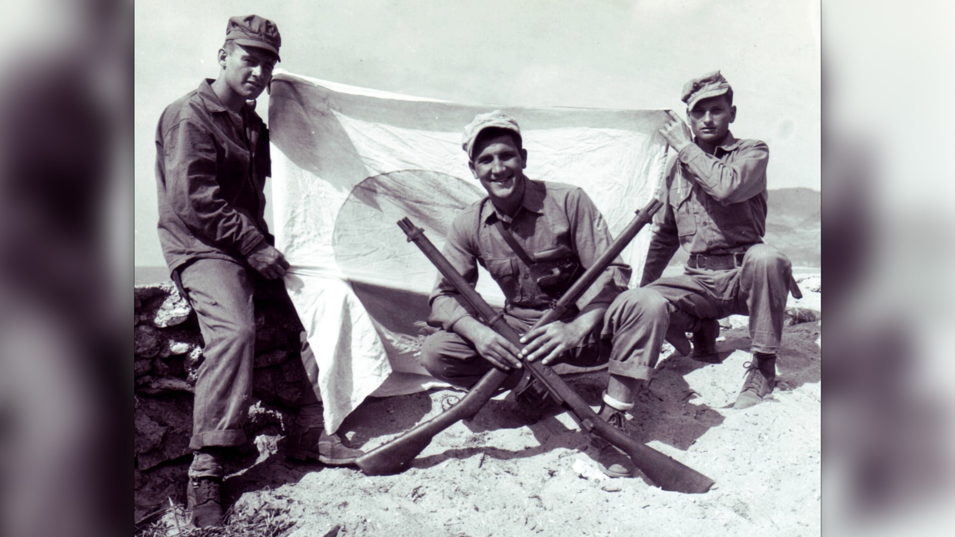 U.S. Marines with Type 22 Murata rifles crossed in front of Japanese flag outdoors
