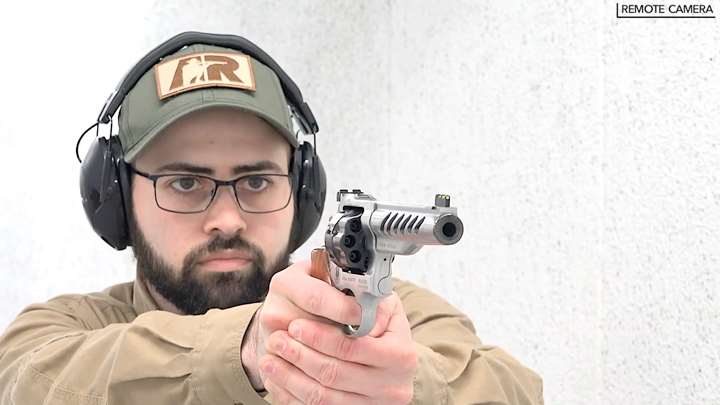 Man with protective shooting gear and ballcap shooting a revolver on a shooting range.