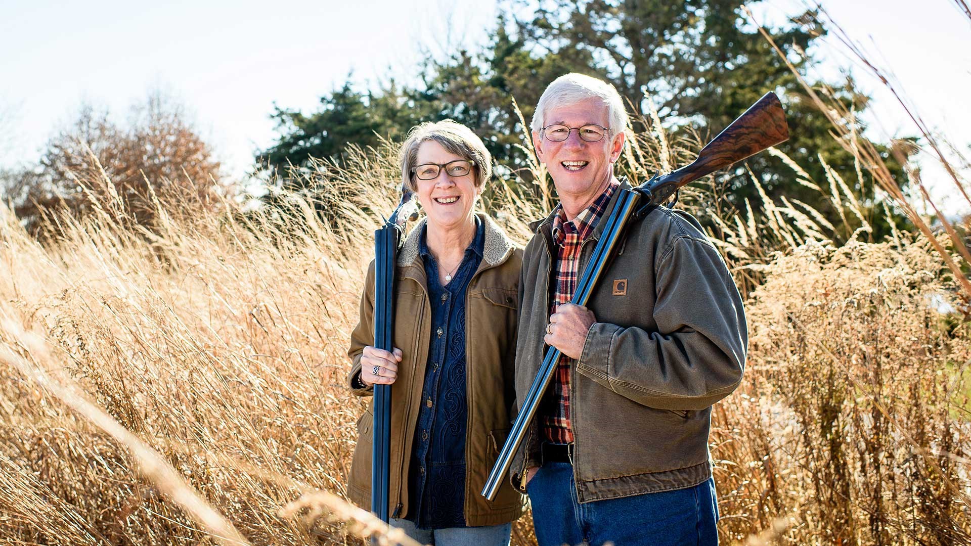 Larry and Brenda Potterfield shown in a grass field, holding shotguns.
