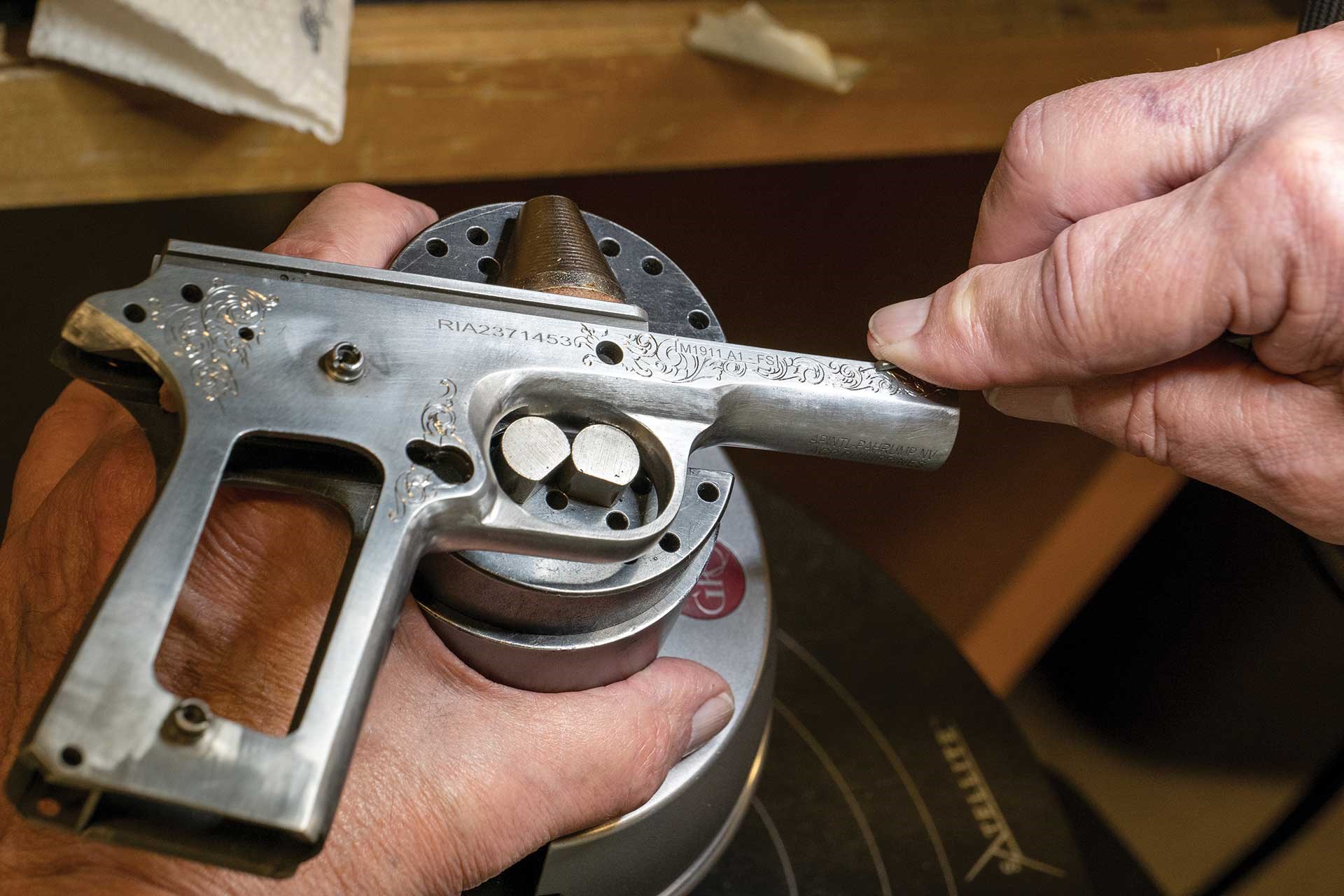 A man works on engraving an M1911 pistol frame.