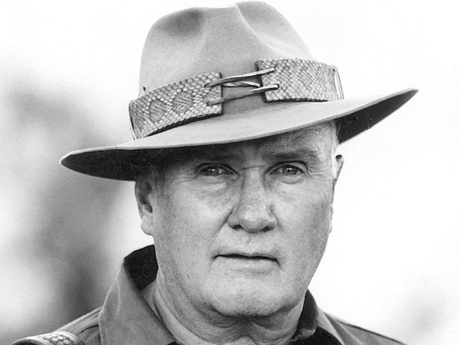 Col. Jeff Cooper wearing a wide-brimmed hat with rattlesnake trim, staring into the camera.