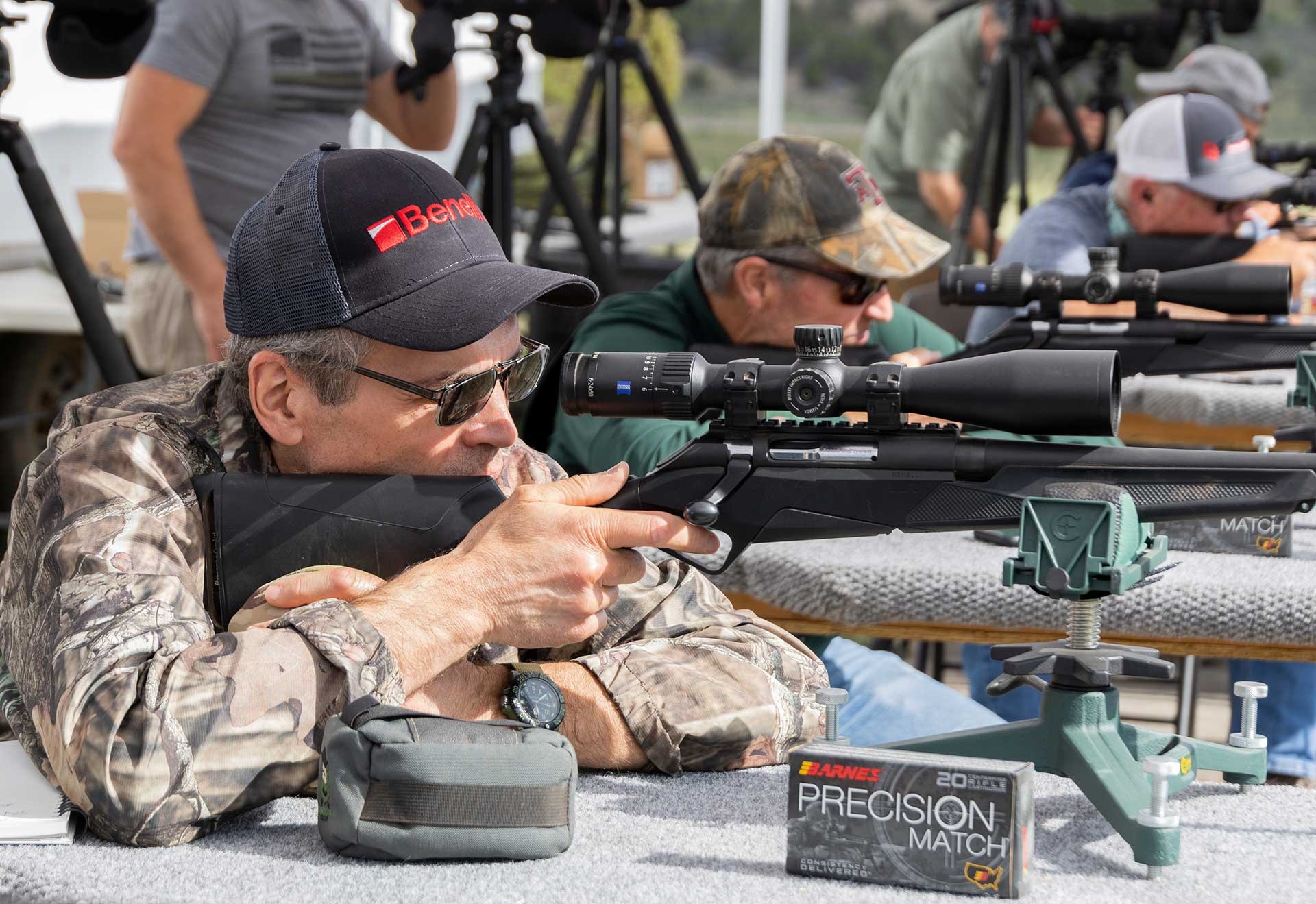 A group of shooters aim their rifles downrange from the bench on a known-distance target range.