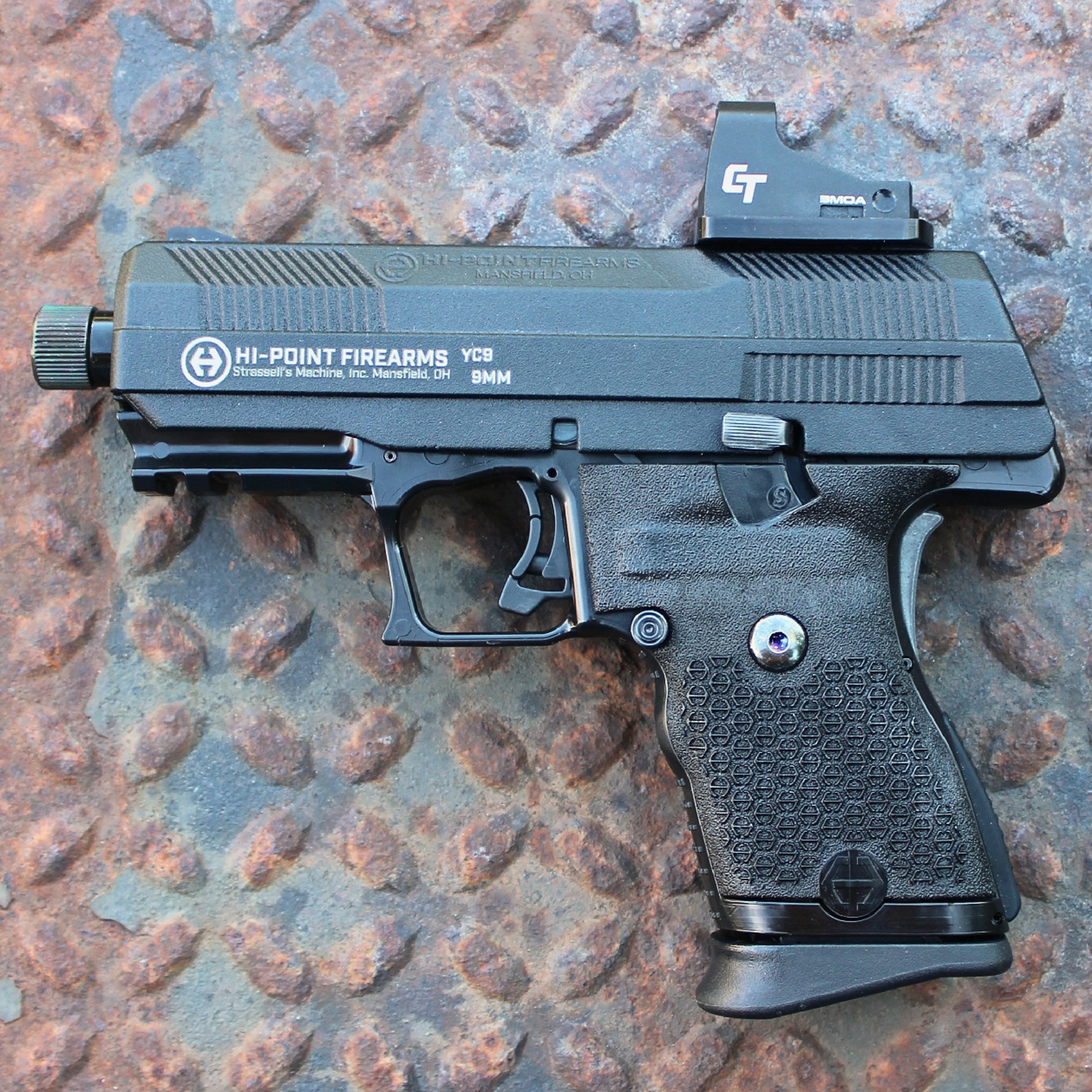 Hi-Point Firearms YC9RD left-side view black pistol handgun 9mm on rusty metal shown with crimson trace red-dot optic