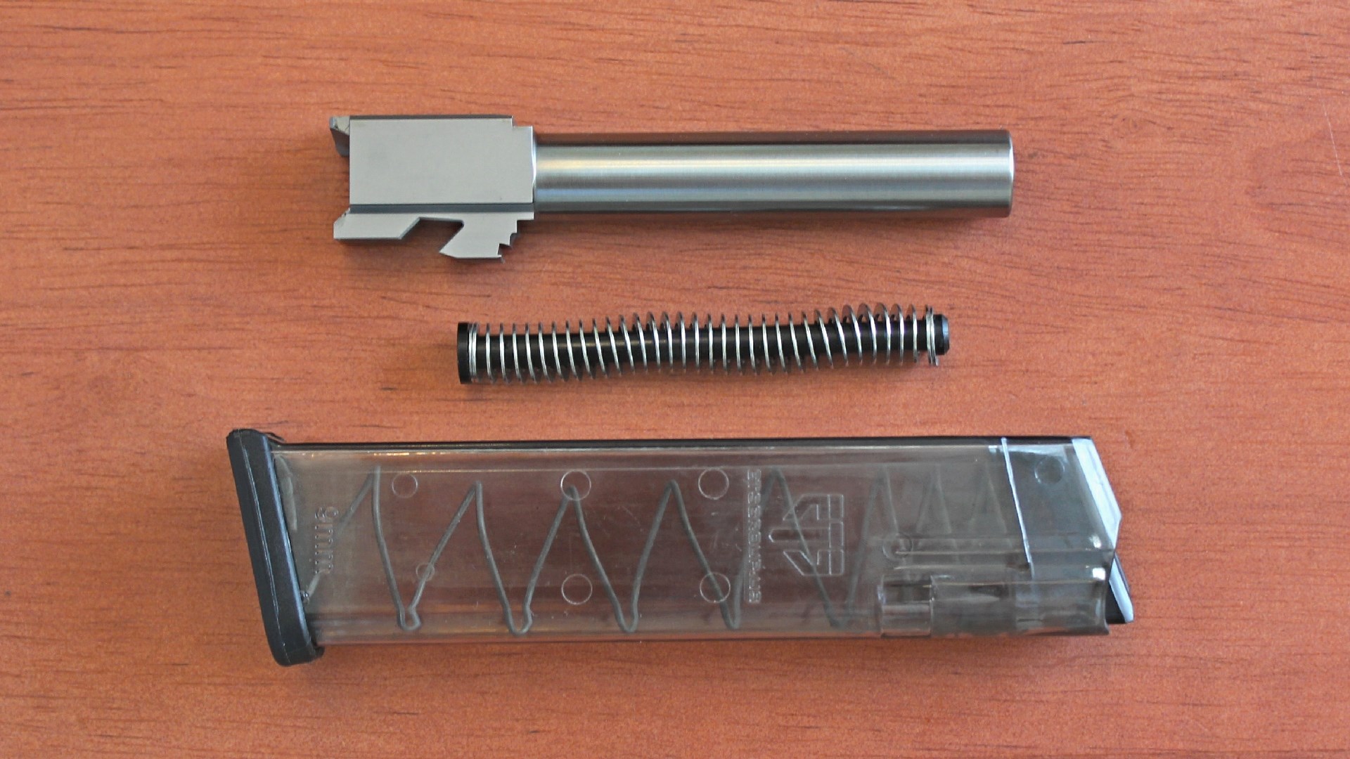 Gun parts barrel recoil spring assembly clear polymer magazine shown on wood table