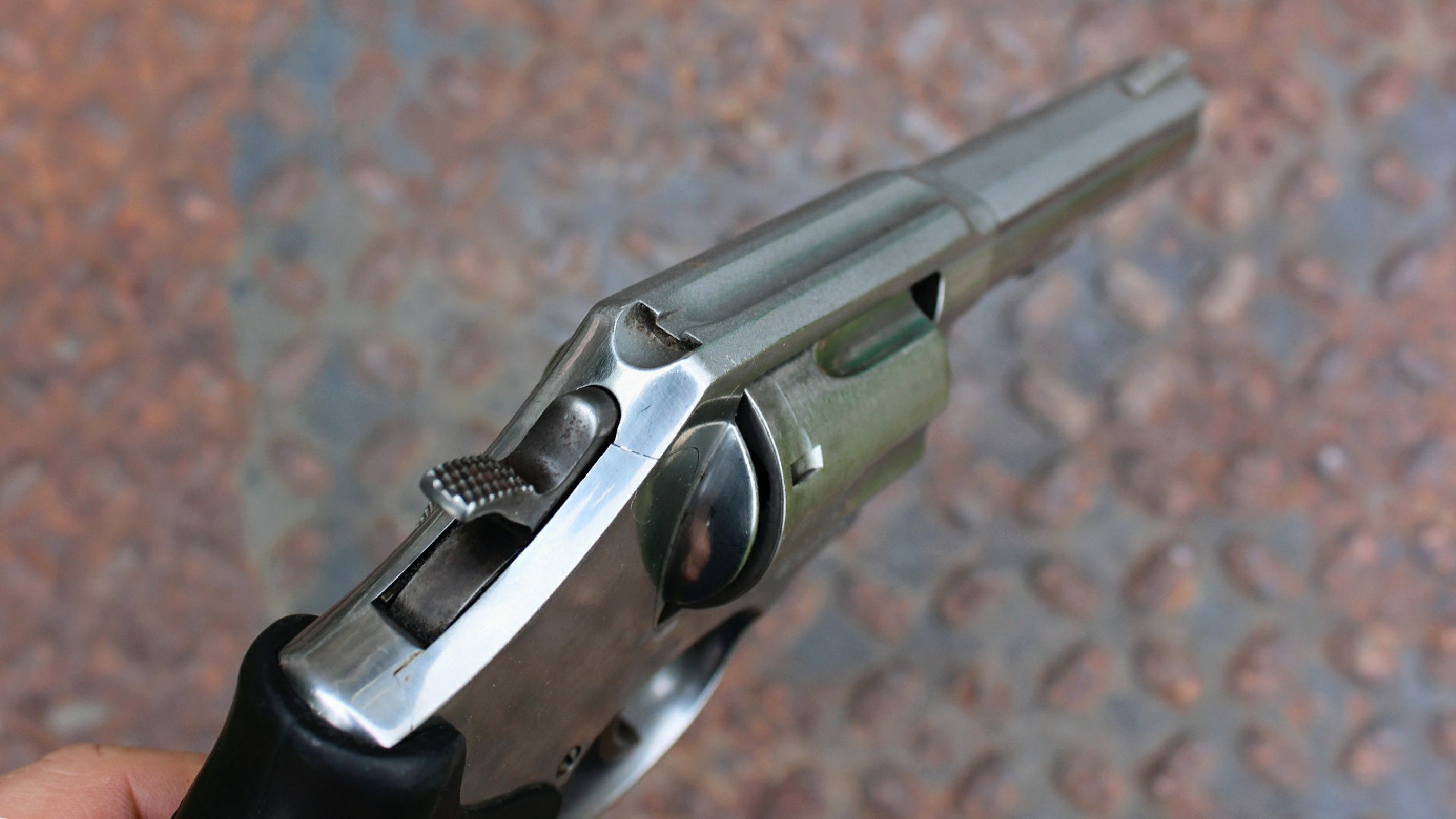 Smith & Wesson stainless steel model 648 revovler top-down right-side quartering view of hammer spur with checkering square-notch rear sight fluted topstrap rusted treadplate background