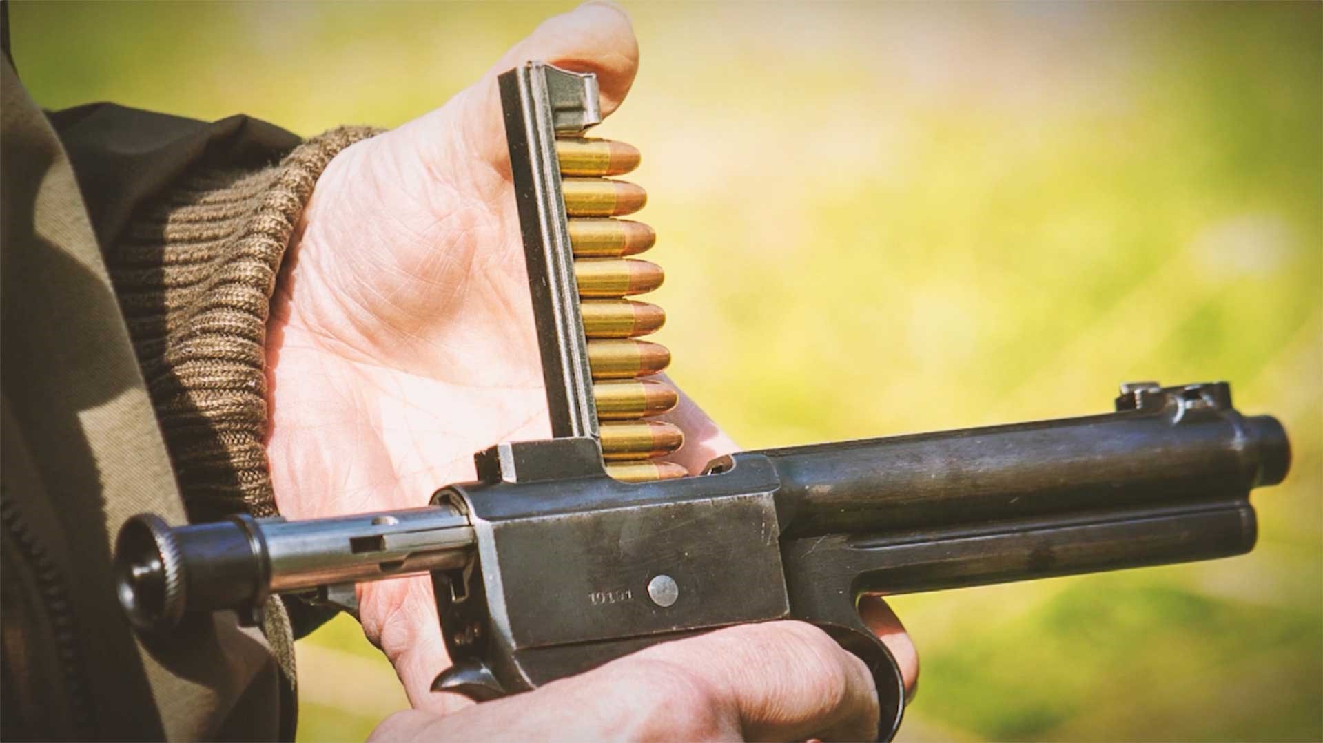 A man loading an M1907 Roth-Steyr pistol using a loading tool.